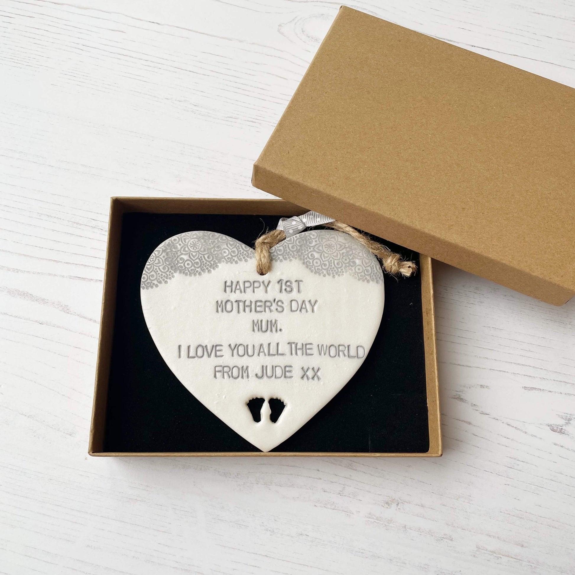 Personalised first Mother’s Day gift, pearlised white clay hanging heart with baby feet cut out at the bottom of the heart and a grey lace edge at the top of the heart, the heart is personalised with HAPPY 1ST MOTHER’S DAY MUM. I LOVE YOU ALL THE WORLD FROM JUDE XX
