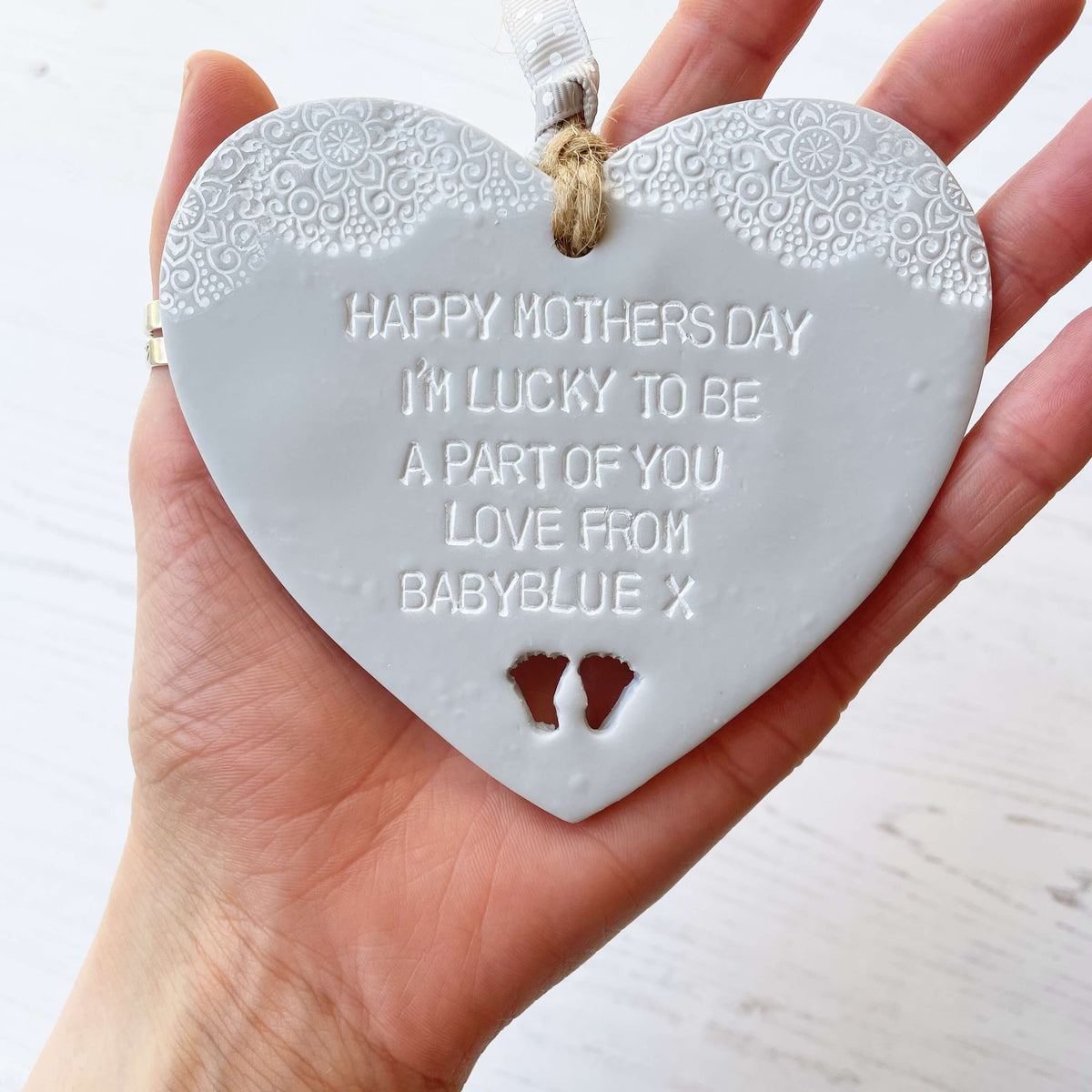 Personalised first Mother’s Day gift, grey clay hanging heart with baby feet cut out at the bottom of the heart and a white lace edge at the top of the heart, the heart is personalised with HAPPY MOTHER’S DAY I’M LUCKY TO BE A PART OF YOU LOVE FROM BABYBLUE X