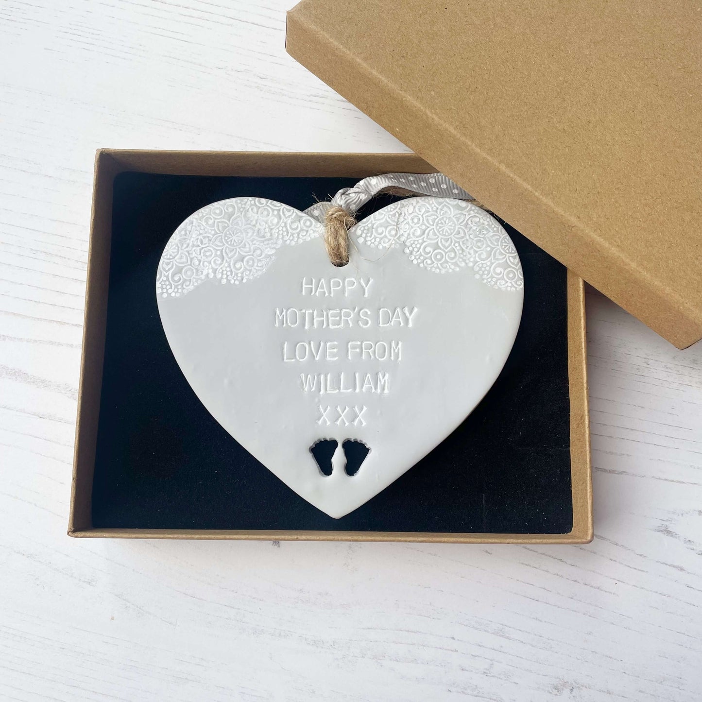 Personalised first Mother’s Day gift, grey clay hanging heart with baby feet cut out at the bottom of the heart and a white lace edge at the top of the heart, the heart is personalised with HAPPY MOTHER’S DAY LOVE FROM WILLIAM XXX