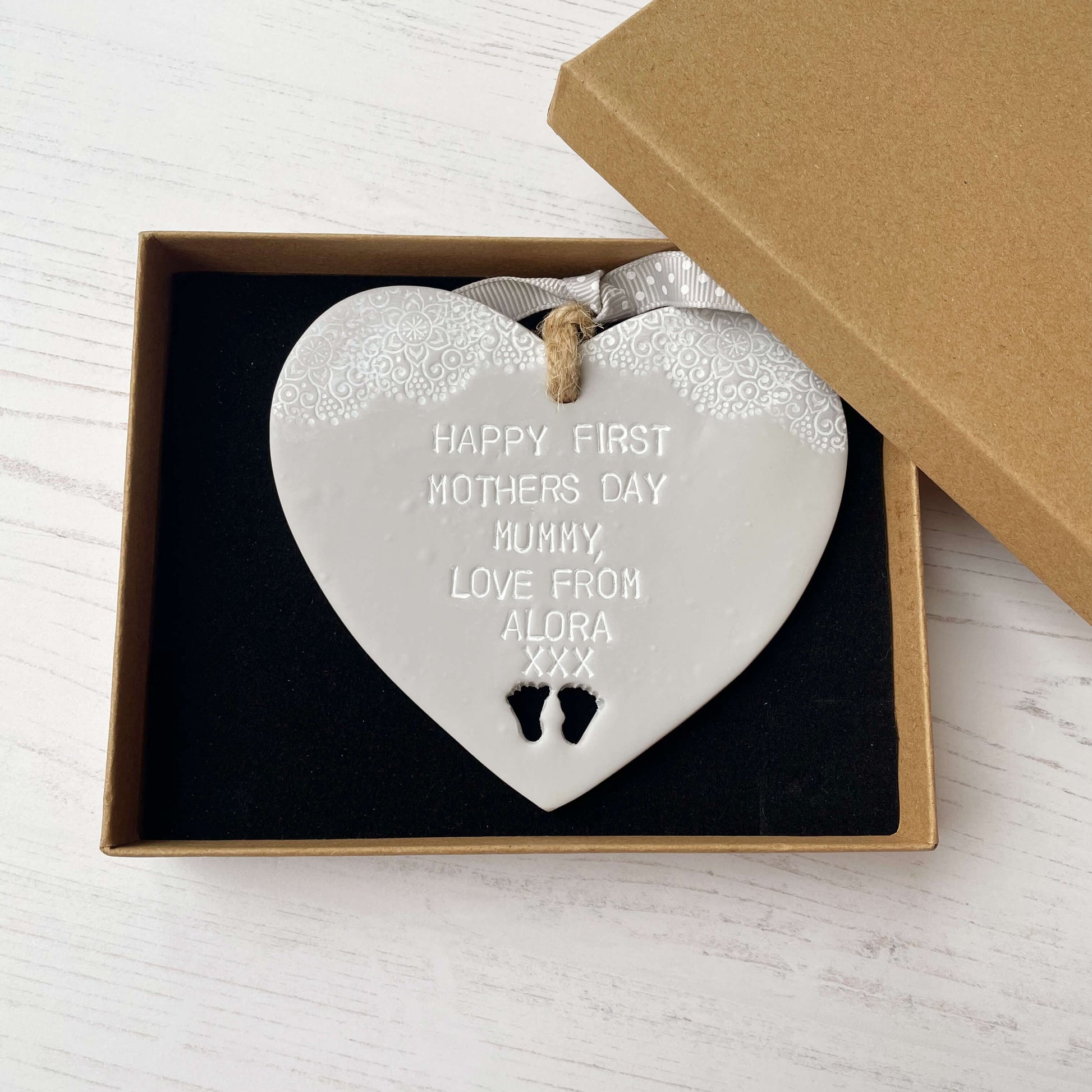 Personalised first Mother’s Day gift, grey clay hanging heart with baby feet cut out at the bottom of the heart and a white lace edge at the top of the heart, the heart is personalised with HAPPY FIRST MOTHERS DAY MUMMY, LOVE FROM ALORA XXX