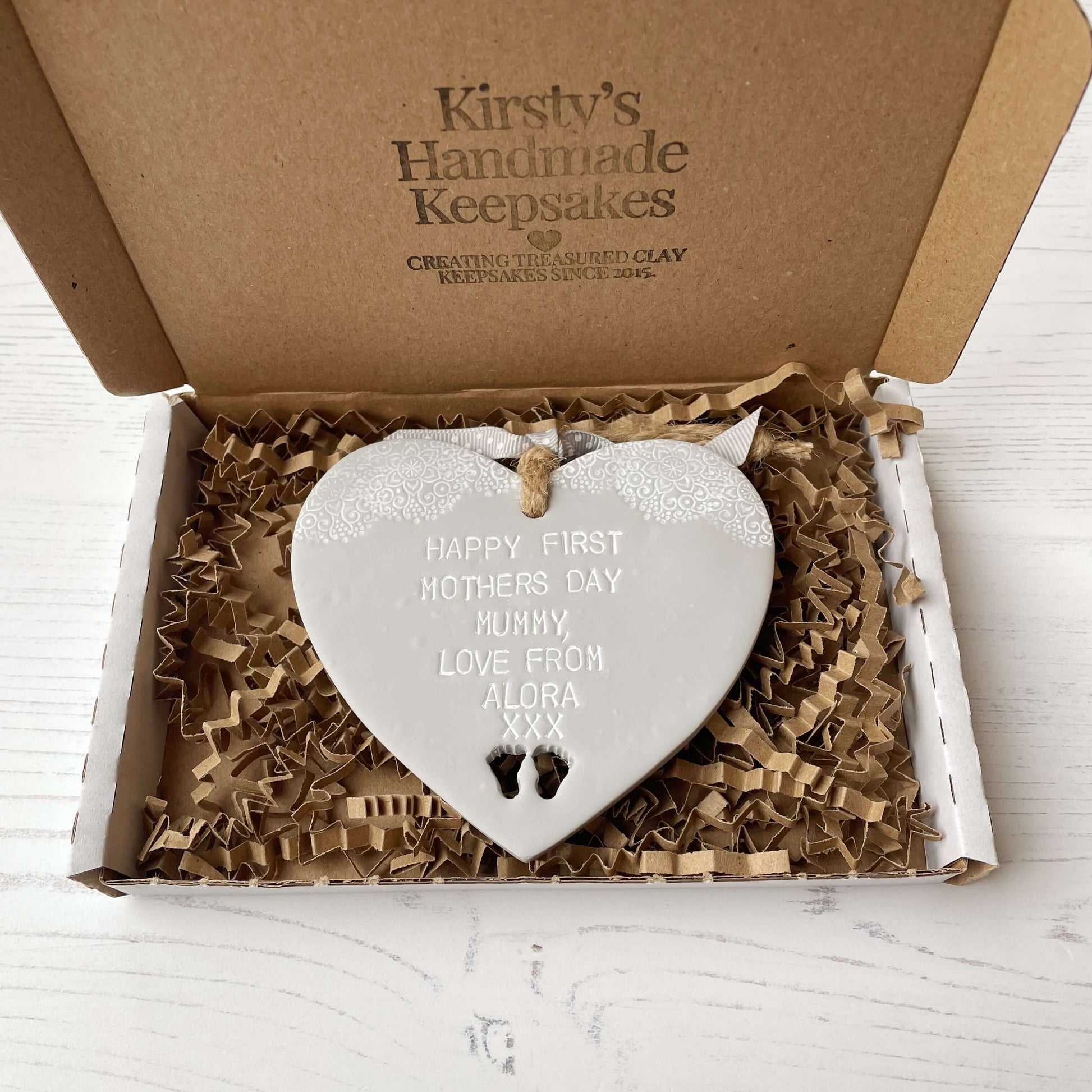 Personalised first Mother’s Day gift, grey clay hanging heart with baby feet cut out at the bottom of the heart and a white lace edge at the top of the heart, the heart is personalised with HAPPY FIRST MOTHERS DAY MUMMY, LOVE FROM ALORA XXX