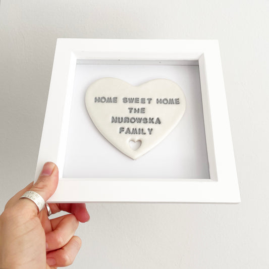 Personalised pearlised white clay heart with a heart cut out at the bottom in a white box frame, the heart is personalised with HOME SWEET HOME THE NUROWSKA FAMILY