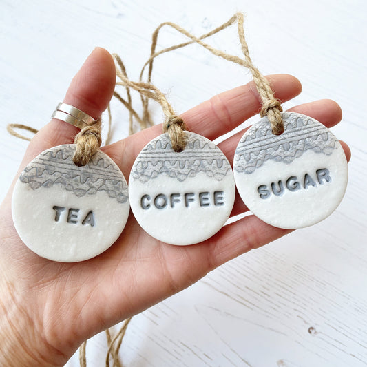 3 round pearlised white clay kitchen canister labels with coffee, tea and sugar stamped on each label in grey with a lace edge top