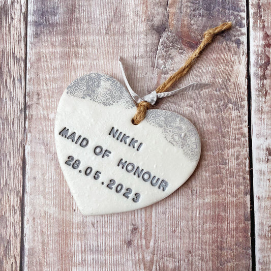 Personalised Bridesmaid thank you gift, pearlised white clay hanging heart with a grey lace edge at the top of the heart, the heart is personalised with NIKKI MAID OF HONOUR 28.05.2023