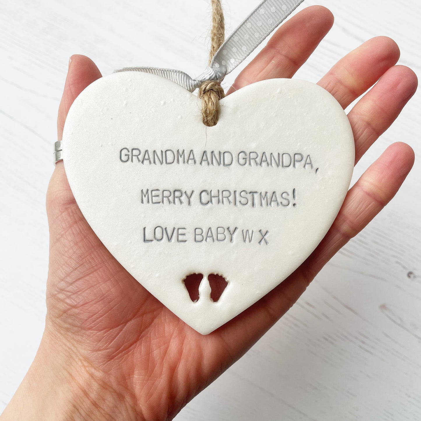 Pearlised white clay hanging heart with baby feet cut out of the bottom and grey personalisation, the heart is personalised with GRANDMA & GRANDPA, MERRY CHRISTMAS! LOVE BABY W X