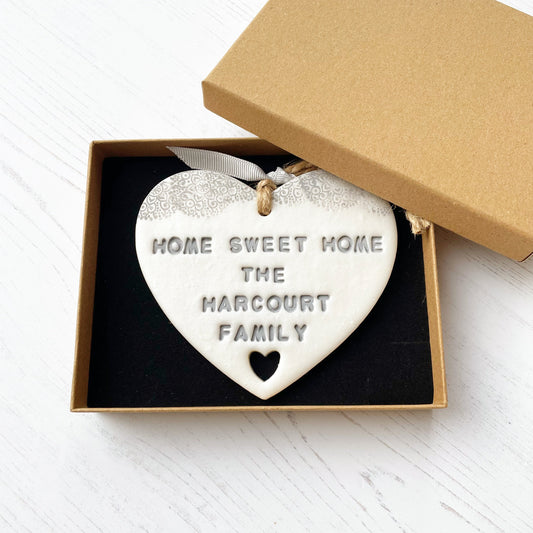 Personalised new home gift pearlised white clay heart with a grey lace edge at the top & a heart cut out at the bottom with twine for hanging personalised with HOME SWEET HOME THE HARCOURT FAMILY in a luxury brown kraft gift box