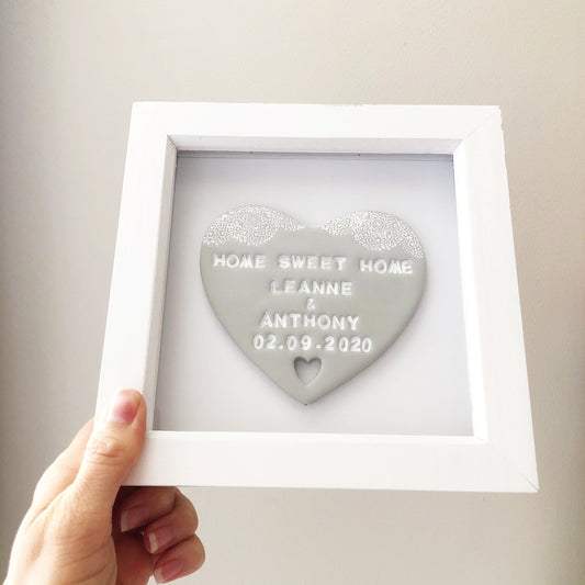 Personalised housewarming new home gift, grey clay heart with a white lace edge at the top of the heart and a heart cut out at the bottom in a white box frame, the heart is personalised with HOME SWEET HOME LEANNE & ANTHONY 02.09.2020