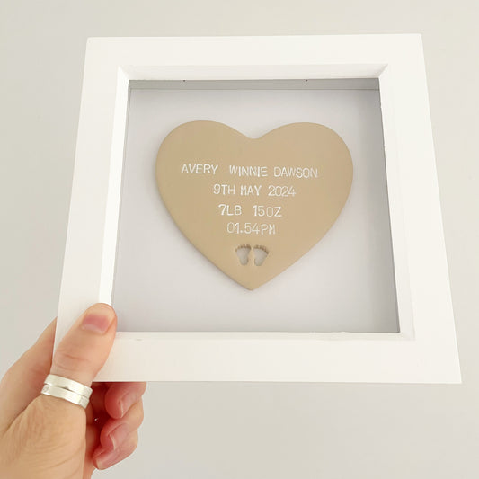 Personalised baby keepsake gift, beige clay heart with baby feet cut out at the bottom of the heart in a white box frame, the heart is personalised with the baby’s name, date of birth, weight and time