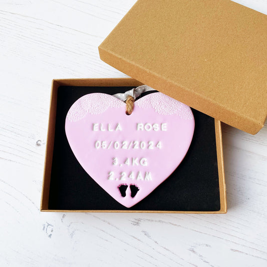 Personalised baby girl keepsake gift, in pink clay hanging heart with a white writing and baby feet cut out at the bottom of the heart, the heart is personalised with ELLIA ROSE 05/02/2024 3.4 KG 2.24 AM In a brown Kraft luxury gift box