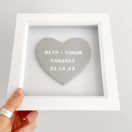 Personalised framed engagement gift, grey clay heart in a white box frame, the heart is personalised with BETH & CONOR ENGAGED 22.06.23