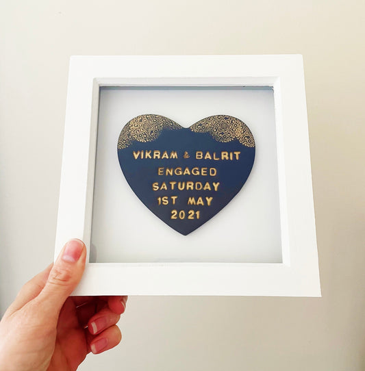 Personalised framed engagement gift, dark blue clay heart with a gold lace edge at the top of the heart in a white box frame, the heart is personalised with VIKRAM & BALRIT ENGAGED SATURDAY 1ST MAY 2021