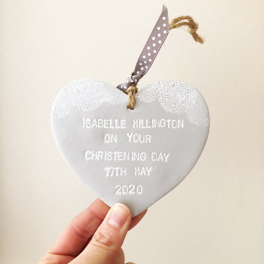 Personalised Christening baptism gift, grey clay hanging heart with a white lace edge at the top of the heart, the heart is personalised with ISABELLE MILLINGTON ON YOUR CHRISTENING DAY 17TH MAY 2020