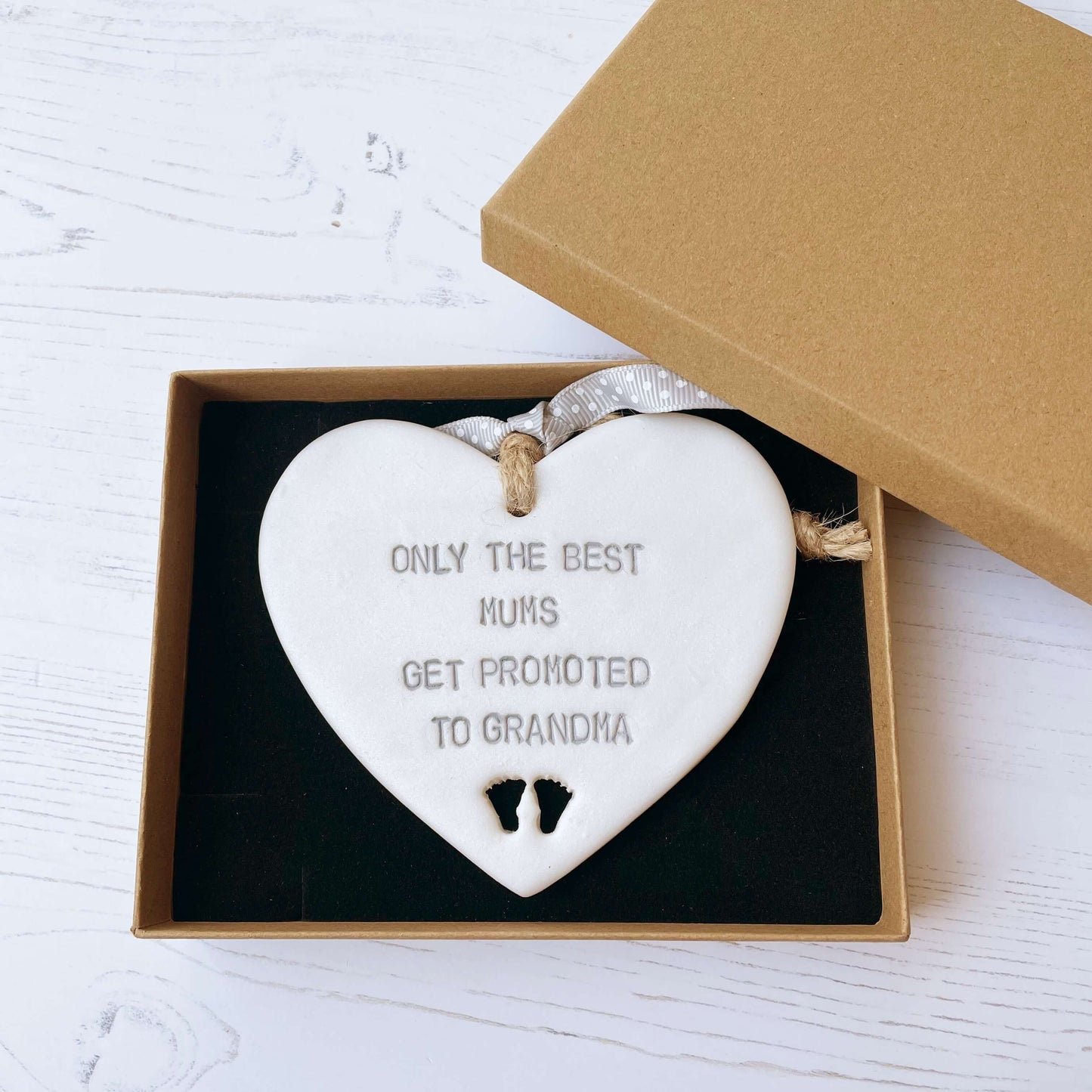 Pearlised white clay hanging heart with baby feet cut out of the bottom and grey personalisation, the heart is personalised with ONLY THE BEST MUMS GET PROMOTED TO GRANDMA