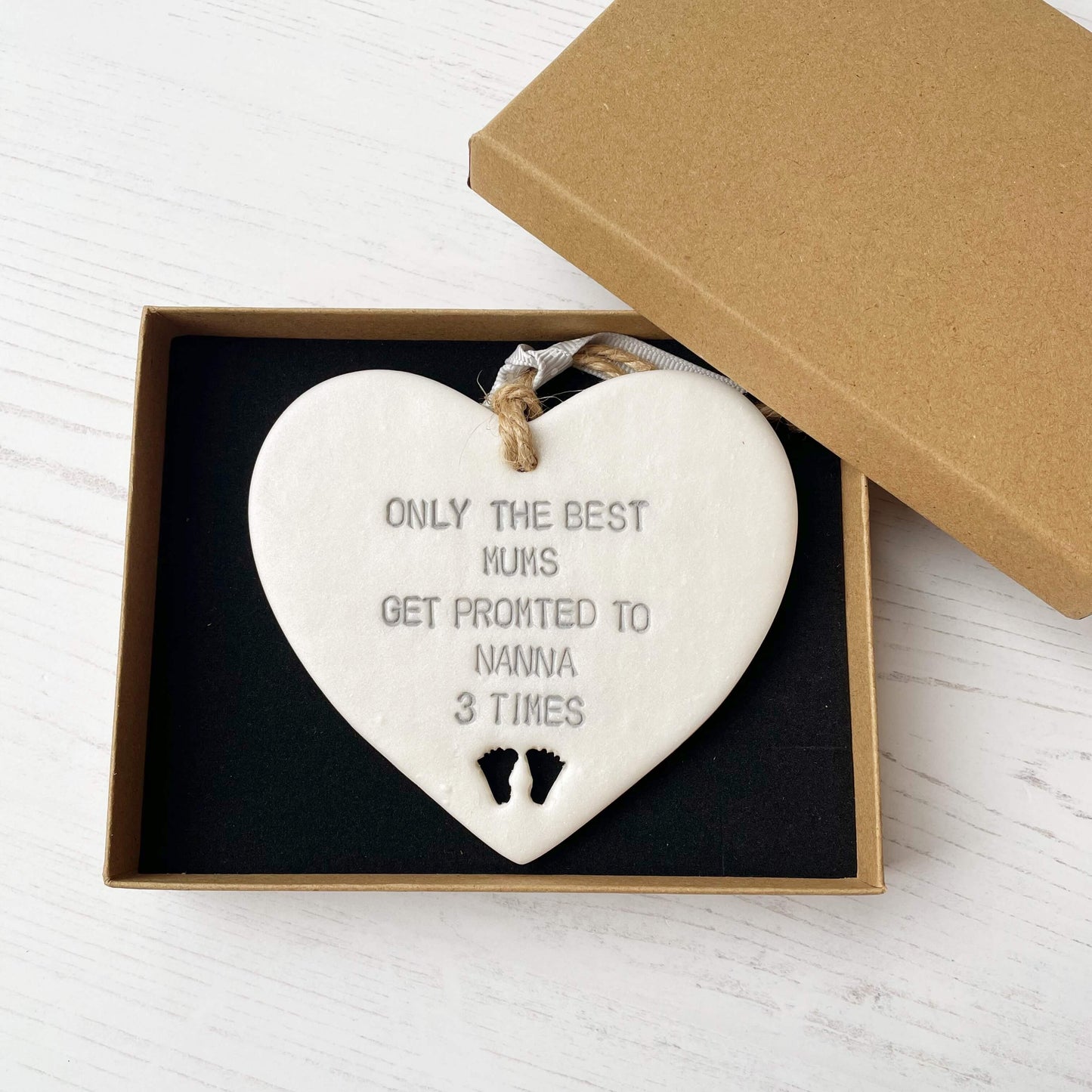 Pearlised white clay hanging heart pregnancy reveal with baby feet cut out of the bottom and grey personalisation, the heart is personalised with ONLY THE BEST MUMS GET PROMOTED TO NANNA 3 TIMES
