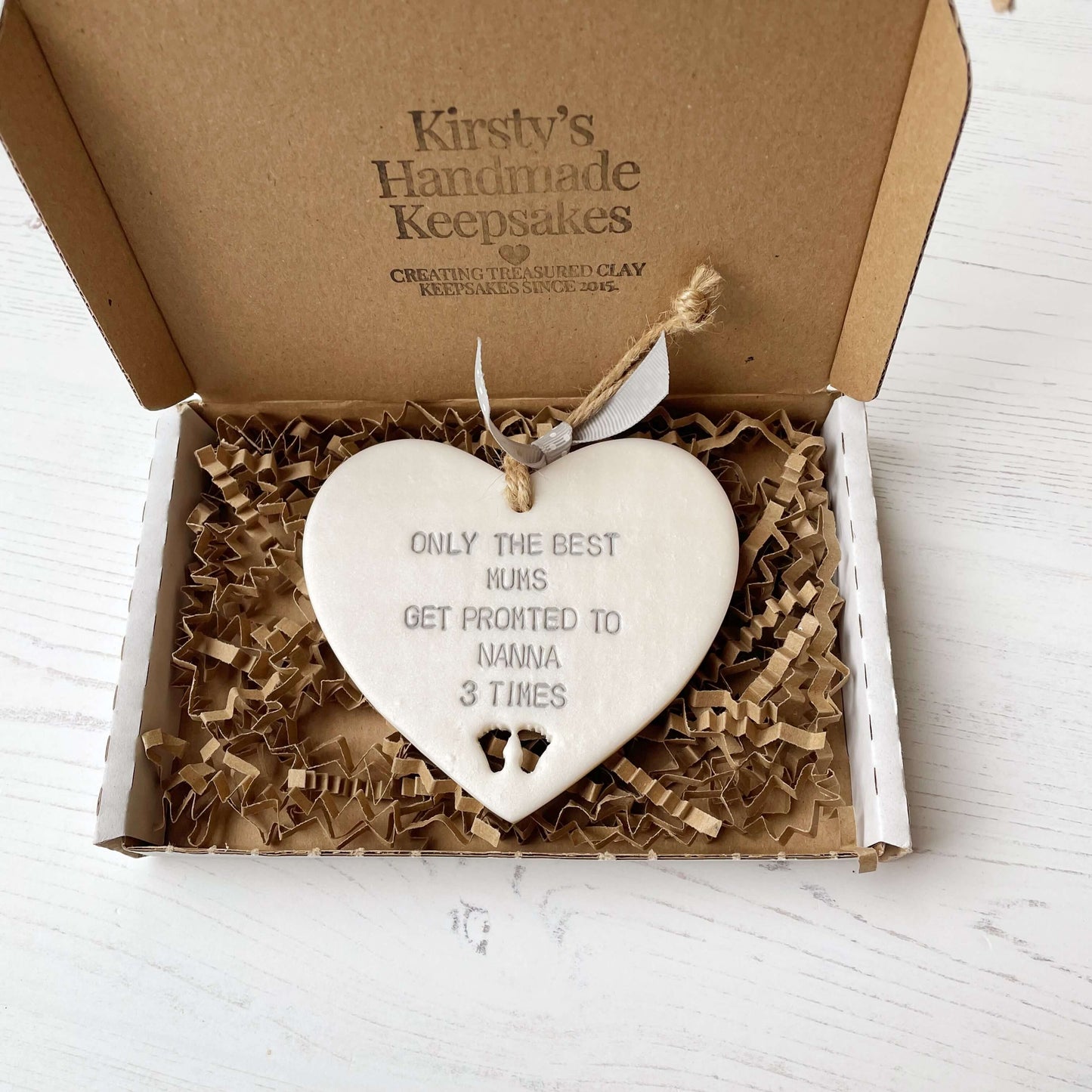 Pearlised white clay hanging heart pregnancy reveal with baby feet cut out of the bottom and grey personalisation, the heart is personalised with ONLY THE BEST MUMS GET PROMOTED TO NANNA 3 TIMES