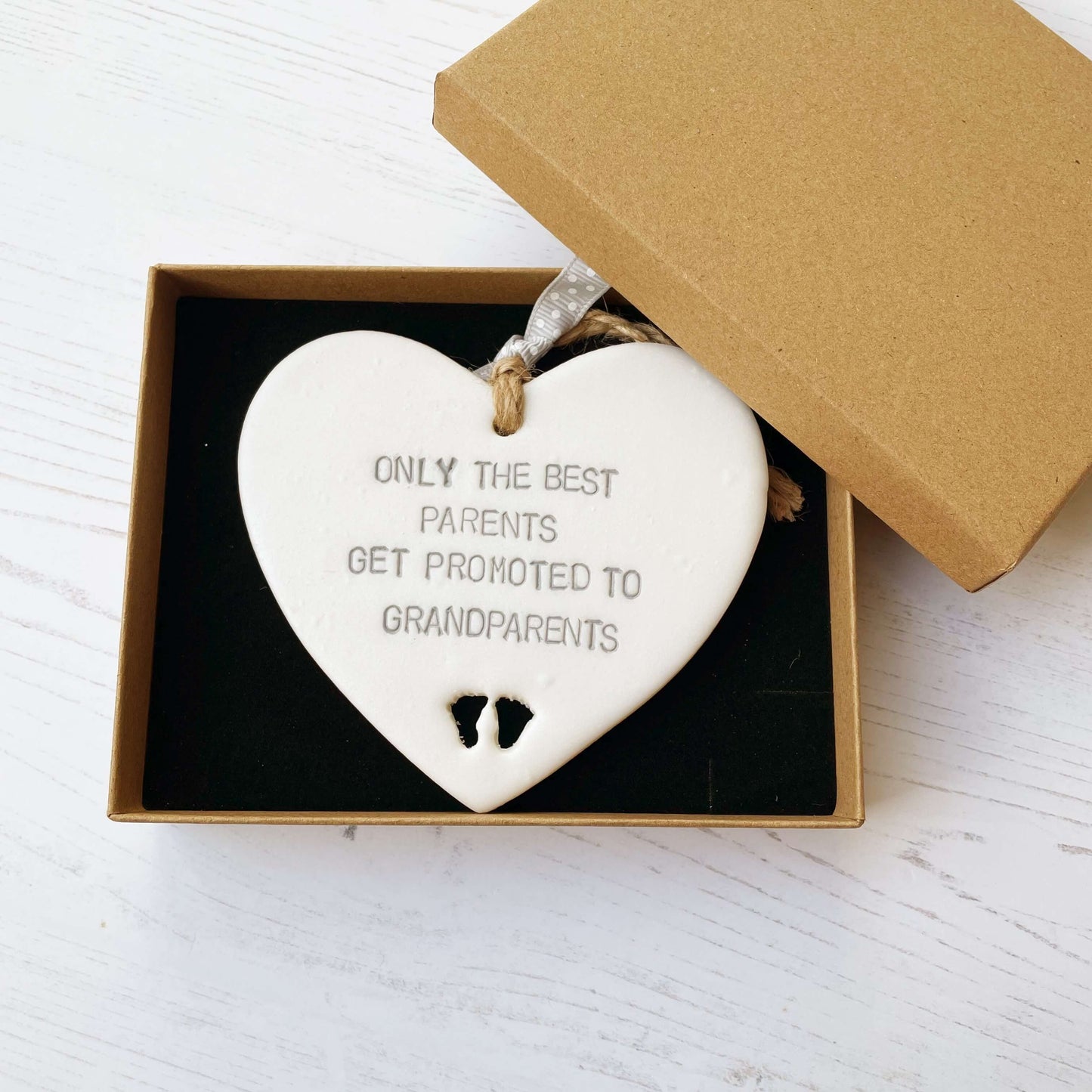 Pearlised white clay hanging heart with baby feet cut out of the bottom and grey personalisation, the heart is personalised with ONLY THE BEST PARENTS GET PROMOTED TO GRANDPARENTS