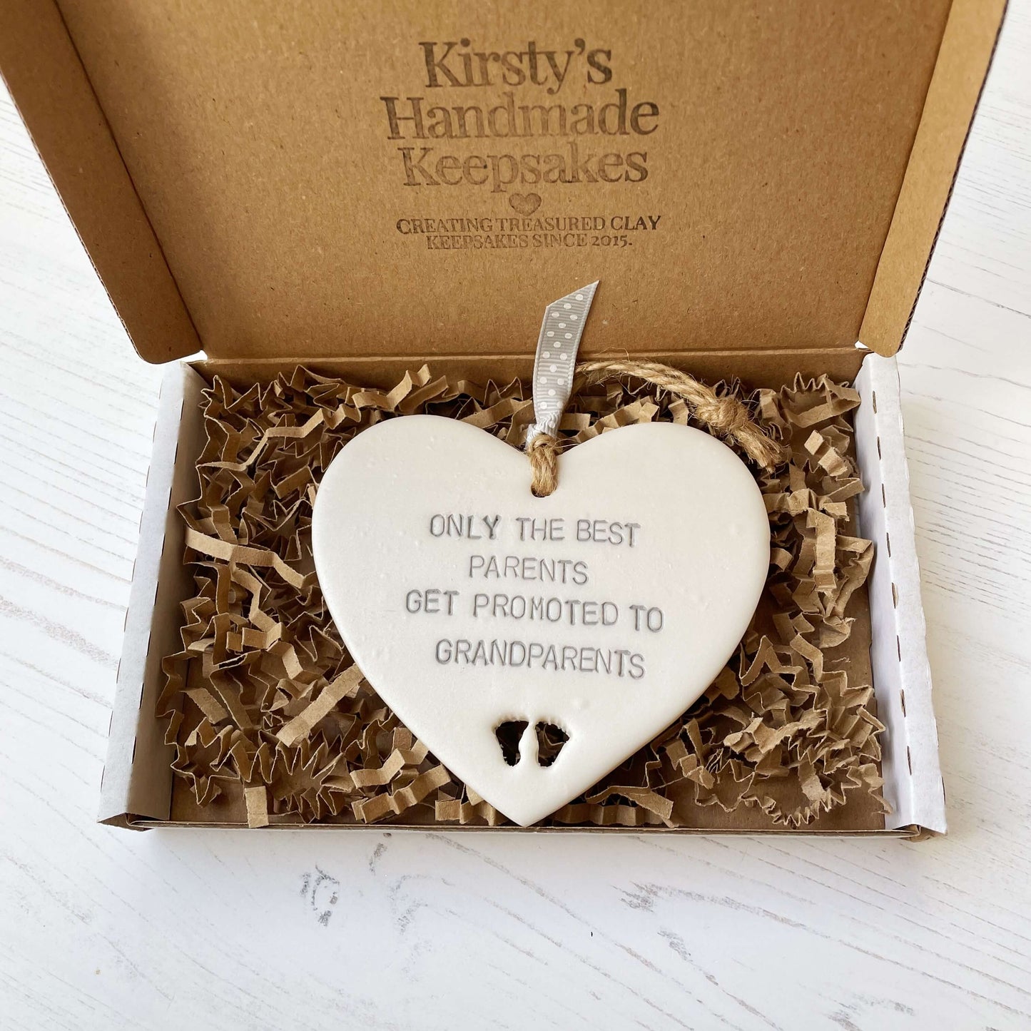 Pearlised white clay hanging heart with baby feet cut out of the bottom and grey personalisation, the heart is personalised with ONLY THE BEST PARENTS GET PROMOTED TO GRANDPARENTS