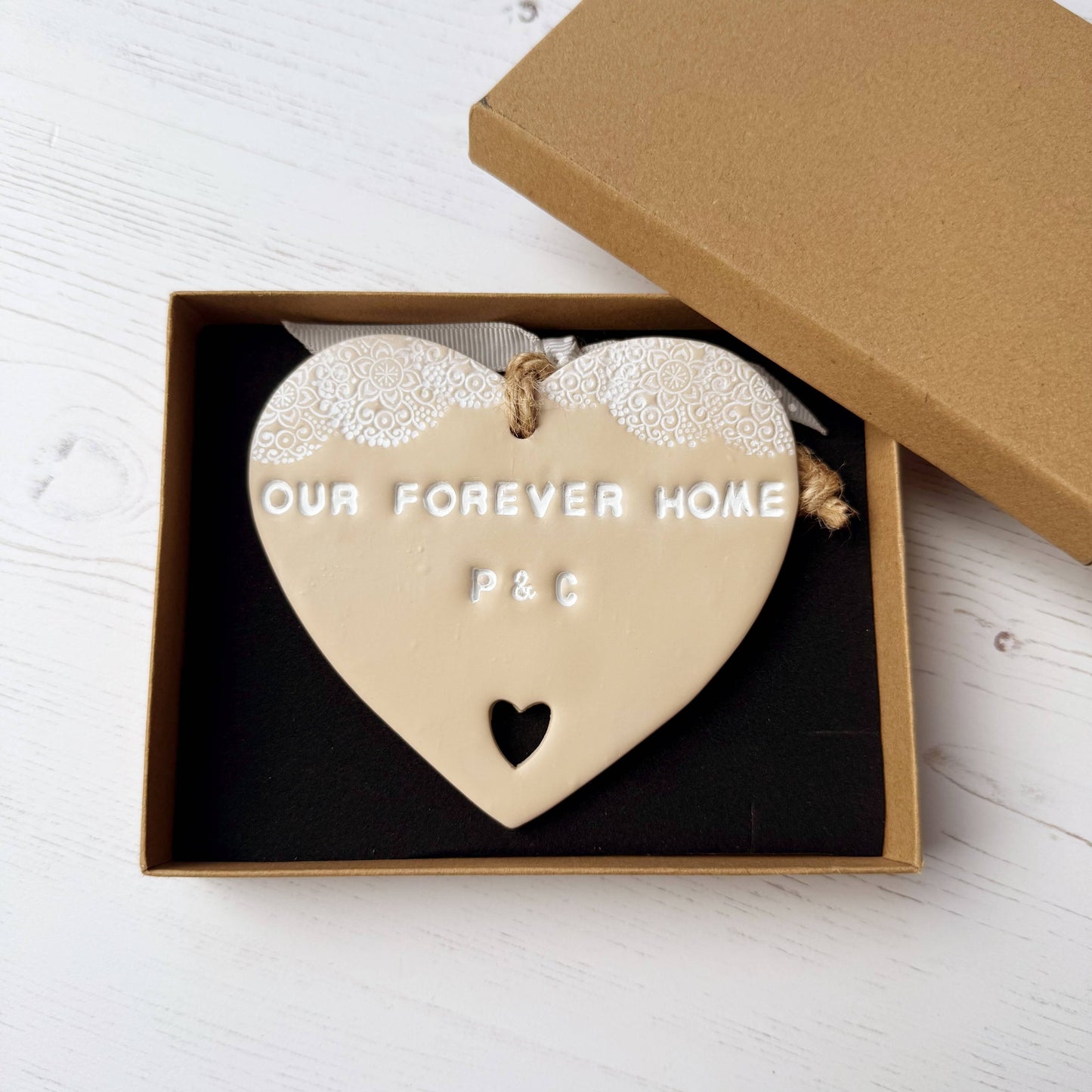 Personalised housewarming new home gift, beige clay heart with a white lace edge at the top of the heart and a heart cut out at the bottom with jute twine for hanging, the heart is personalised with OUR FOREVER HOME P & C