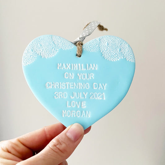 Personalised Christening baptism gift, pastel blue clay hanging heart with a white lace edge at the top of the heart, the heart is personalised with MAXIMILIAN ON YCUR CHRISTENING DAY 3RD JULY 2021 LOVE MORGAN
