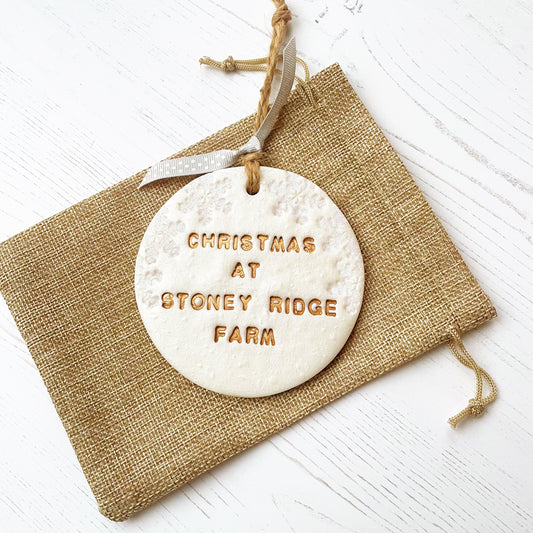Personalised first Christmas in our new home bauble ornament, pearlised white round clay with CHRISTMAS AT STONEY RIDGE FARM in gold paint, decorated with 3 iridescent glitter snowflakes on either side of the bauble