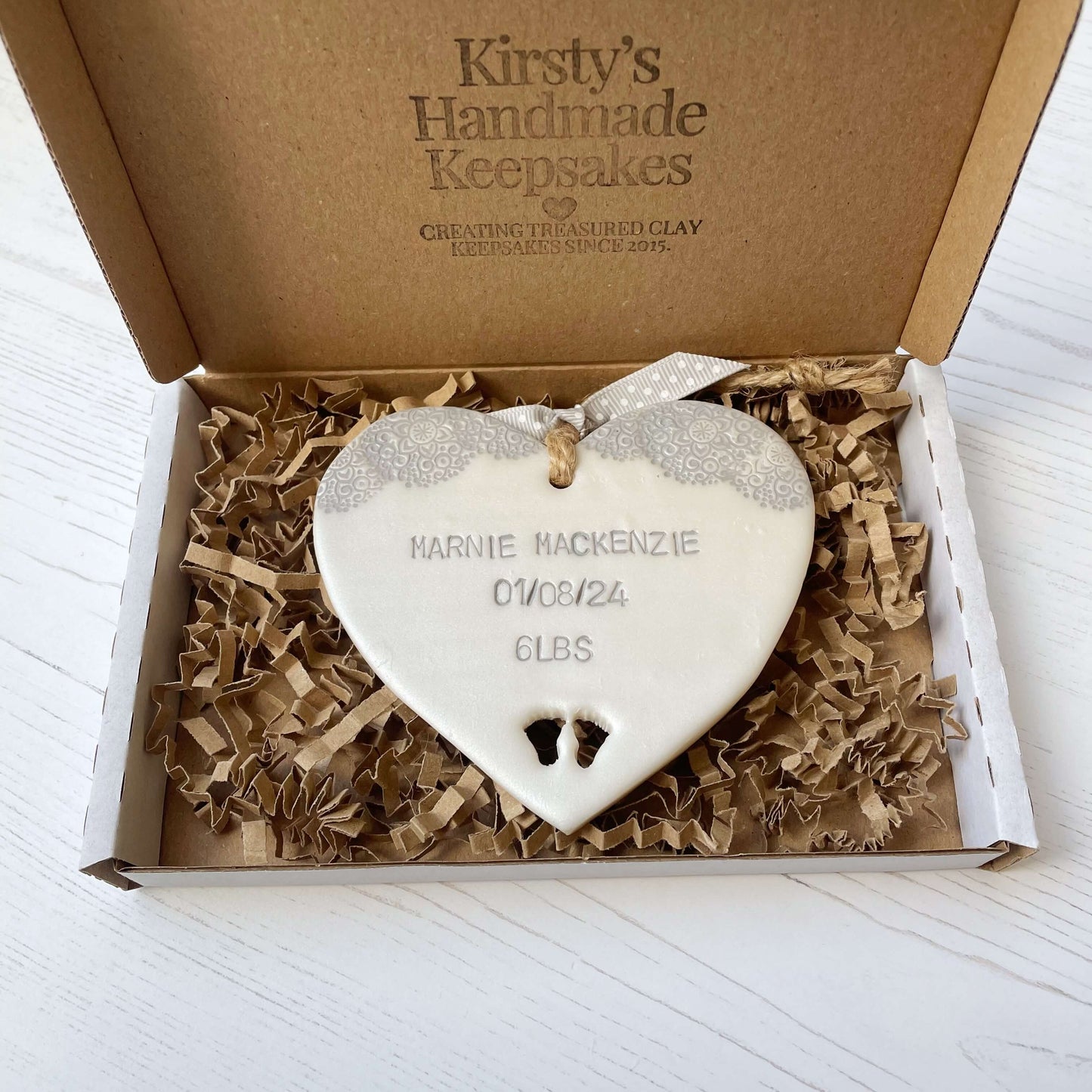 Personalised baby keepsake gift, pearlised white clay hanging heart with a grey lace edge top and baby feet cut out at the bottom of the heart, the heart is personalised with the baby’s name, date of birth and weight