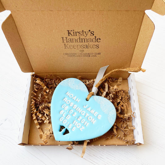 Personalised baby keepsake heart in pastel blue with white lace edge detail to the top and baby feet cut out at the bottom, personalised with Noah James Rossington 06.03.2011 6LB 11OZ 00:55 In a white postal box with brown Kraft shredded zigzag paper