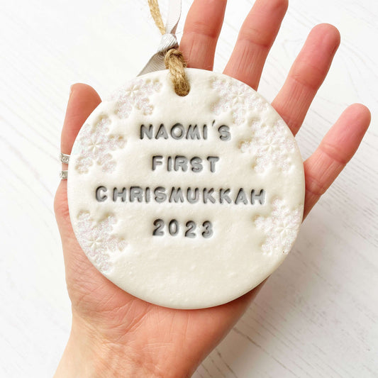 Personalised baby's first Christmas bauble ornament, pearlised white round clay with PIPPA’S FIRST CHRISTMAS 2023 in grey paint, decorated with 3 iridescent glitter snowflakes on either side of the bauble