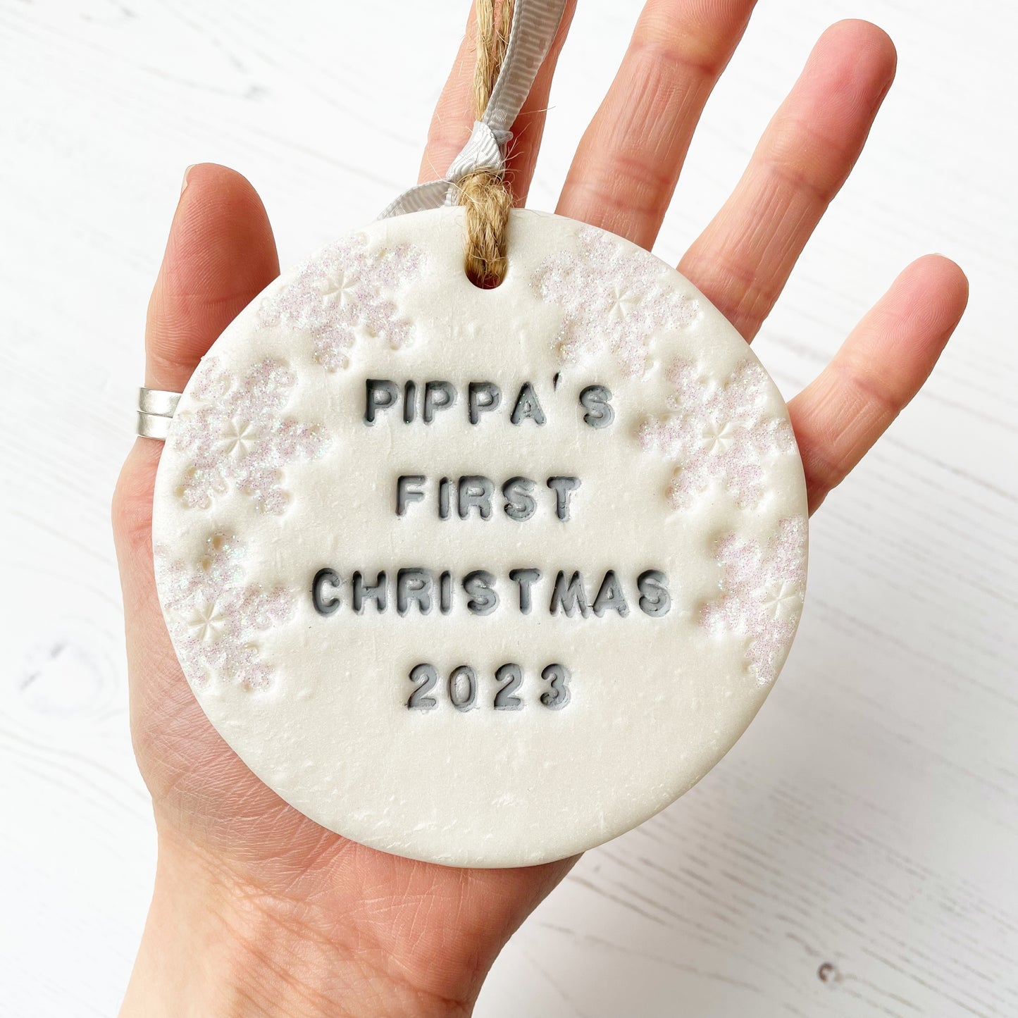 Personalised baby's first Christmas bauble ornament, pearlised white round clay with PIPPA’S FIRST CHRISTMAS 2023 in grey paint, decorated with 3 iridescent glitter snowflakes on either side of the bauble