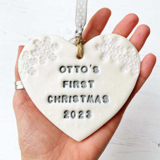 Personalised baby's first Christmas heart ornament, pearlised white clay with OTTO'S FIRST CHRISTMAS 2023 painted grey, decorated with 2 iridescent glitter snowflakes on either side of the top of the heart