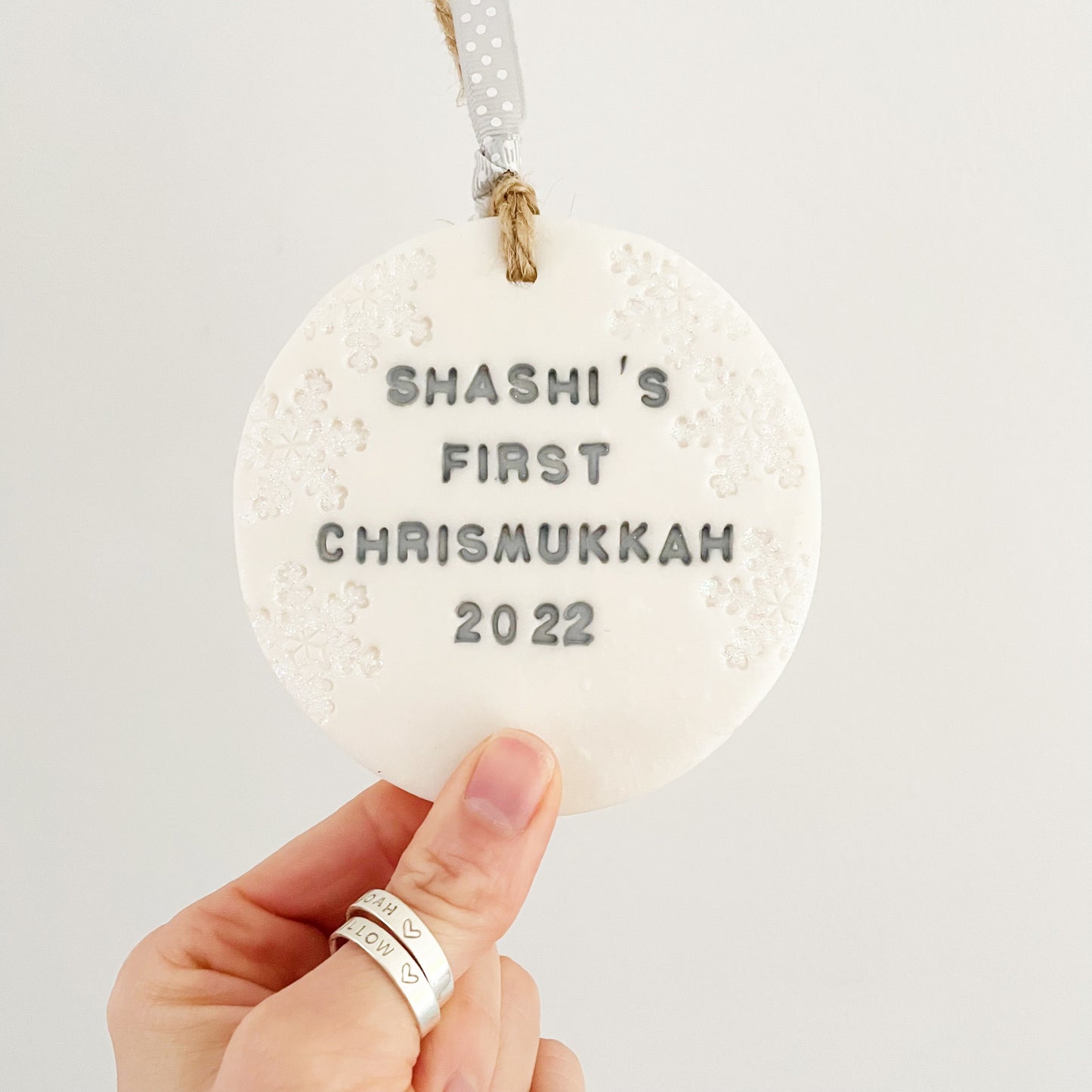 Personalised baby's first Christmas bauble ornament, pearlised white round clay with SHASHI’S FIRST CHRISMUKKAH 2022 in grey paint, decorated with 3 iridescent glitter snowflakes on either side of the bauble