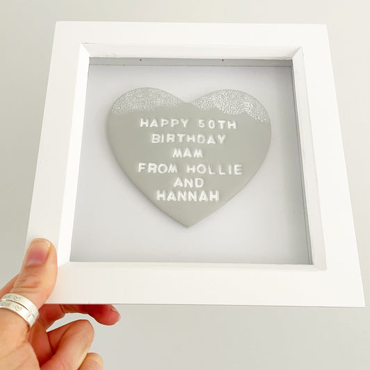 Personalised framed birthday gift, grey clay heart with a white lace edge at the top of the heart in a white box frame, the heart is personalised with HAPPY 50TH BIRTHDAY MAM FROM HOLLIE AND HANNAH