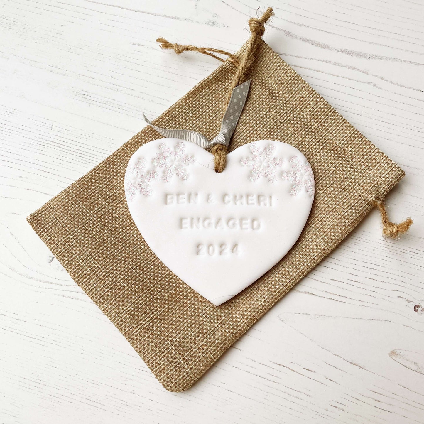 Personalised first Christmas engaged heart ornament, glitter white clay with BEN & CHERI ENGAGED 2024 (text not painted), decorated with 2 iridescent glitter snowflakes on either side of the top of the heart