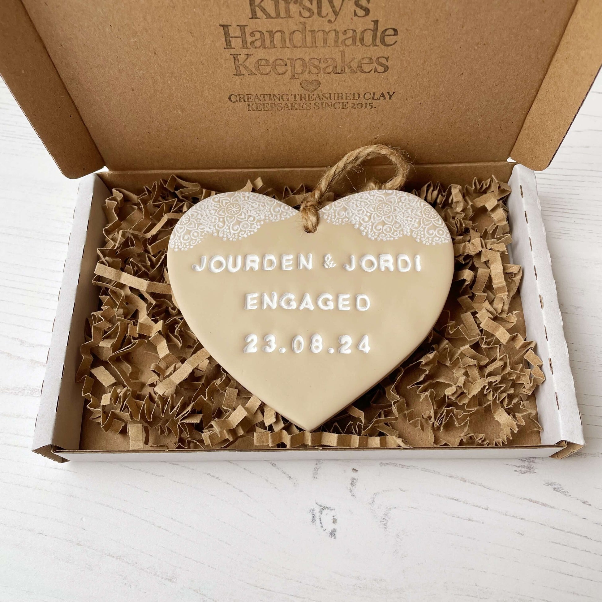 Personalised engagement gift, beige clay heart with a white lace edge at the top of the heart with jute twine for hanging, the heart is personalised with JOURDEN & JORDI ENGAGED 23.08.24