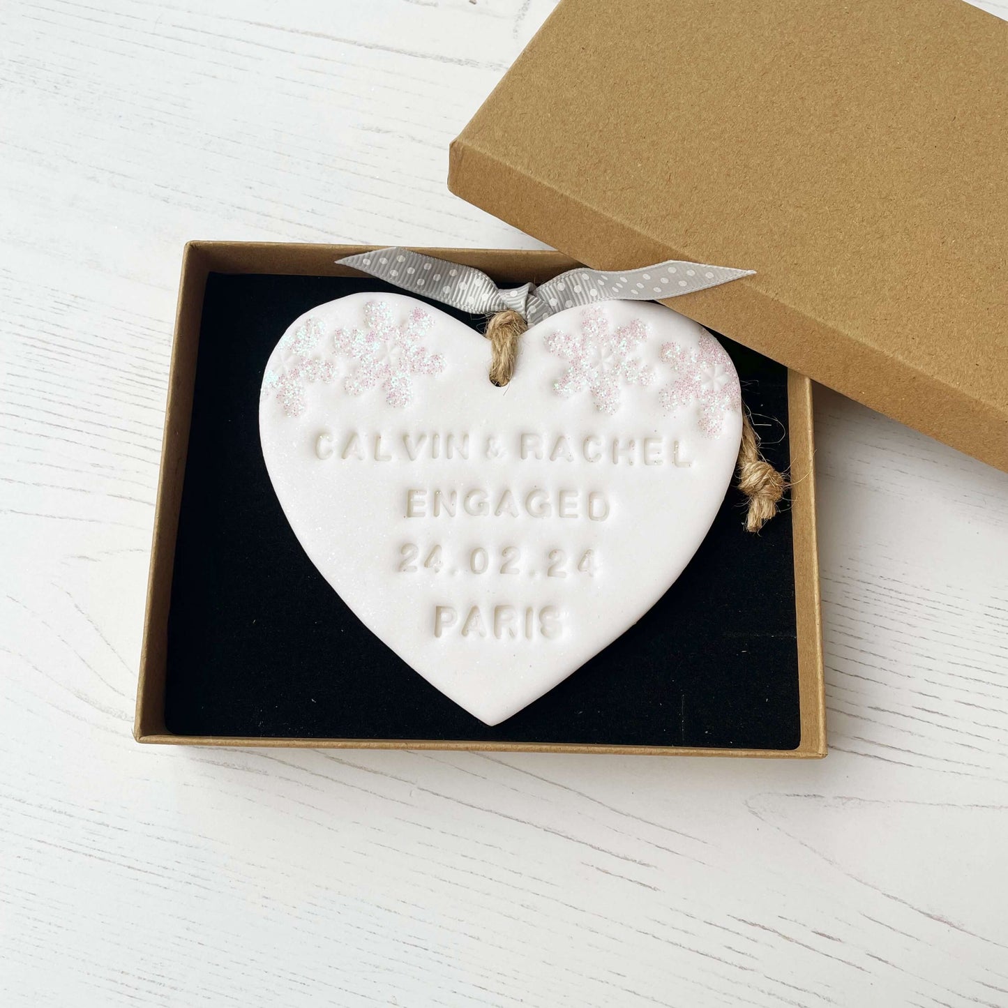 Personalised first Christmas engaged heart ornament, glitter white clay with CALVIN & RACHEL ENGAGED 24.02.24 PARIS (text not painted), decorated with 2 iridescent glitter snowflakes on either side of the top of the heart