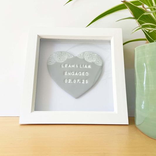 Personalised framed engagement gift, grey clay heart with a white lace edge at the top of the heart in a white box frame, the heart is personalised with LEAH & LIAM ENGAGED 02.07.25