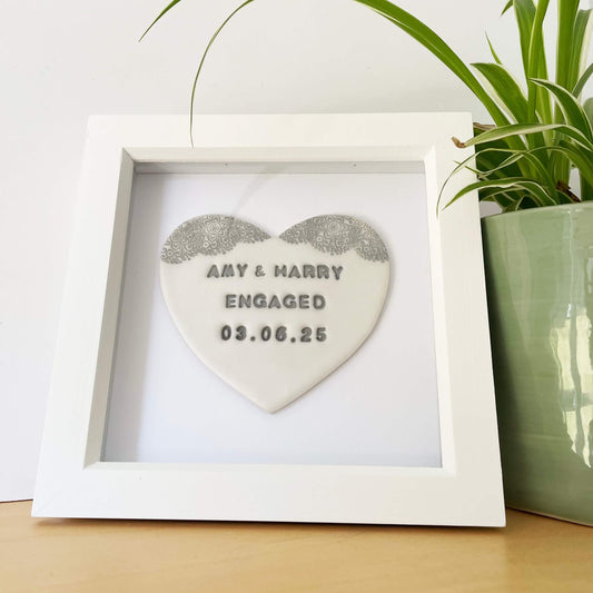 Personalised framed engagement gift, pearlised white clay heart with a white lace edge at the top of the heart in a white box frame, the heart is personalised with AMY & HARRY ENGAGED 03.06.25