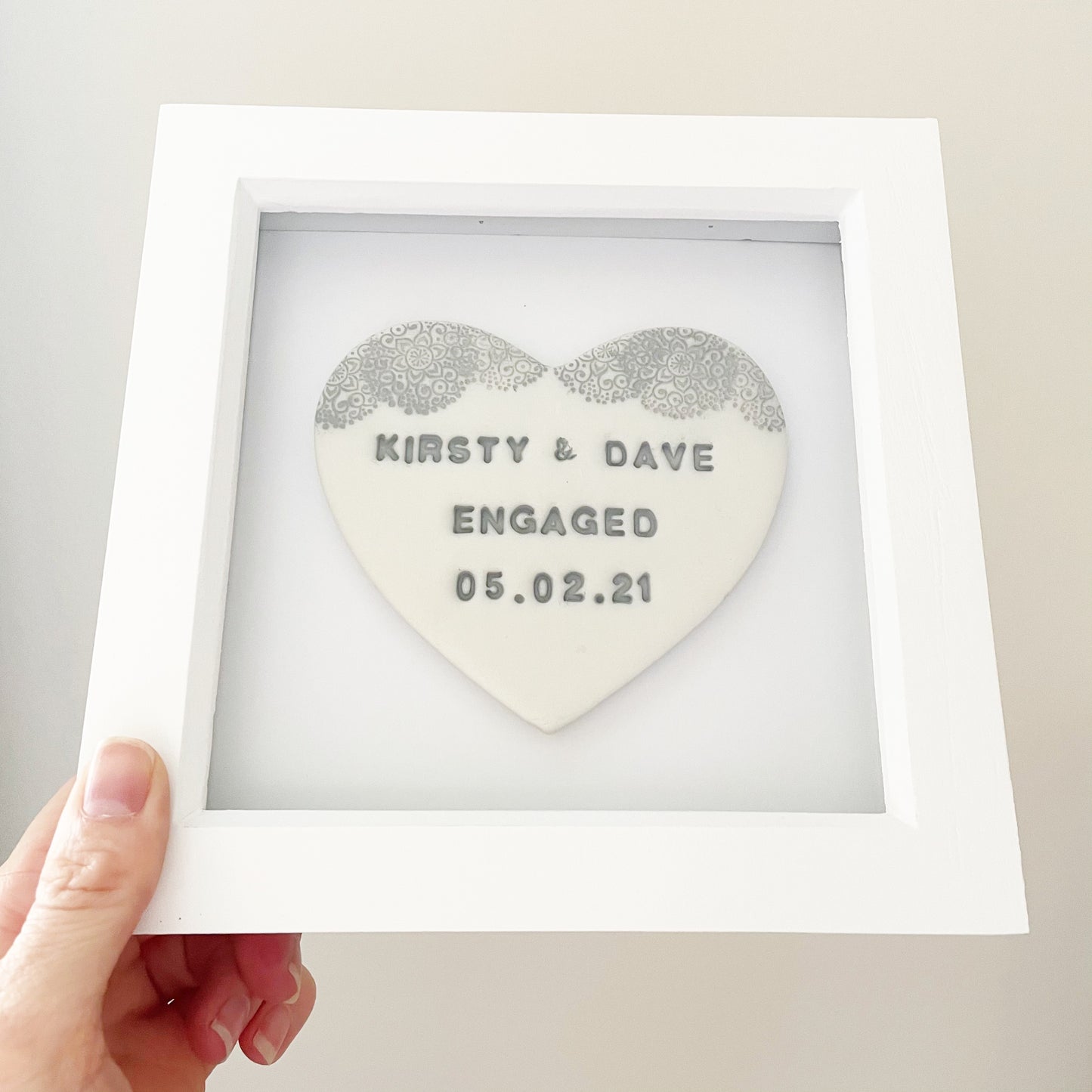 Personalised framed engagement gift, pearlised white clay heart with a white lace edge at the top of the heart in a white box frame, the heart is personalised with KIRSTY & DAVE ENGAGED 05.02.21