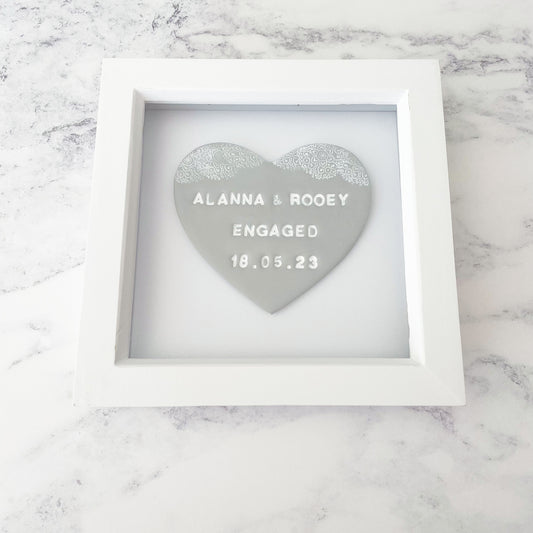 Personalised framed engagement gift, grey clay heart with a white lace edge at the top of the heart in a white box frame, the heart is personalised with ALANNA & ROOEY ENGAGED 18.05.23
