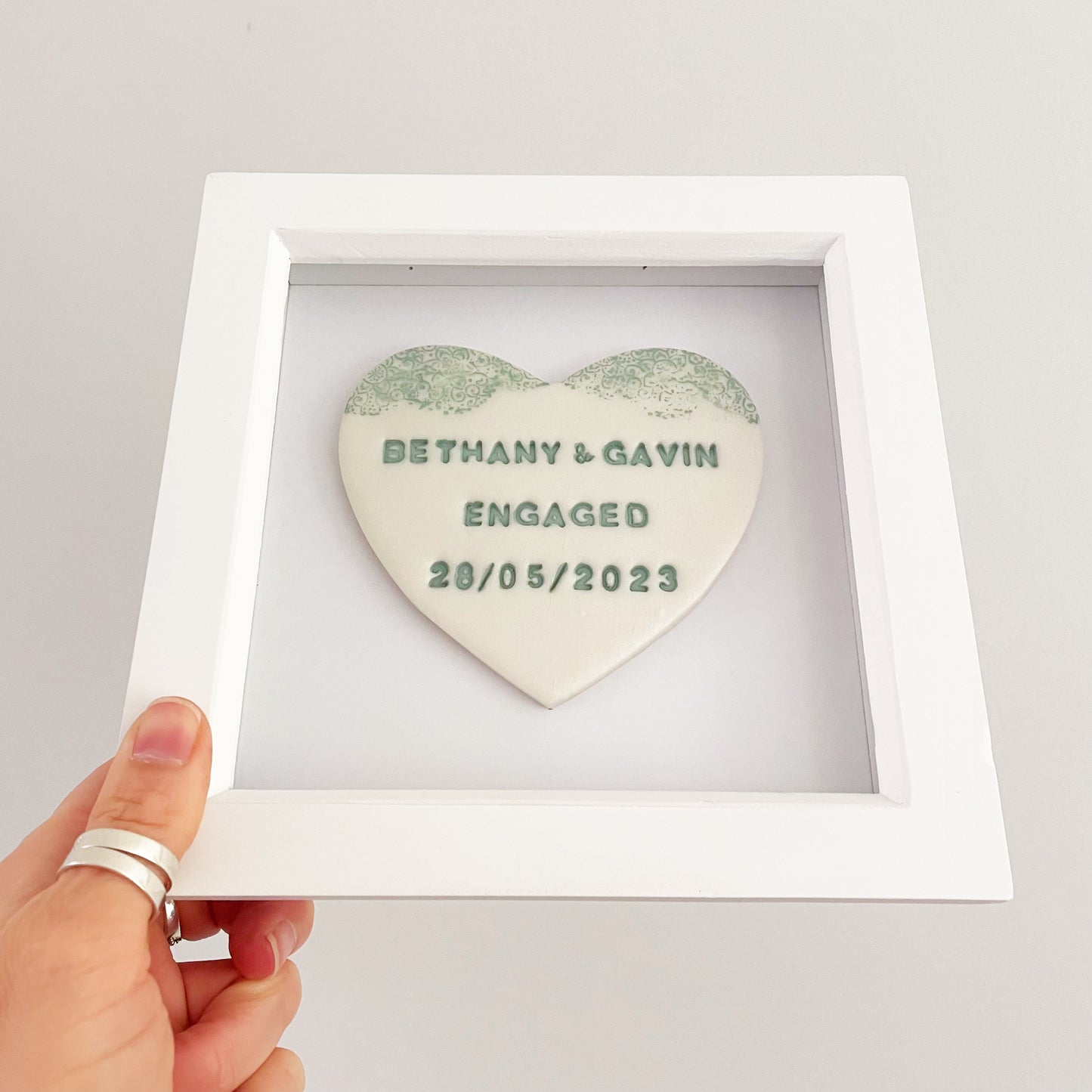 Personalised framed engagement gift, pearlised white clay heart with a white lace edge at the top of the heart in a white box frame, the heart is personalised with BETHANY & GAVIN ENGAGED 28/05/2023