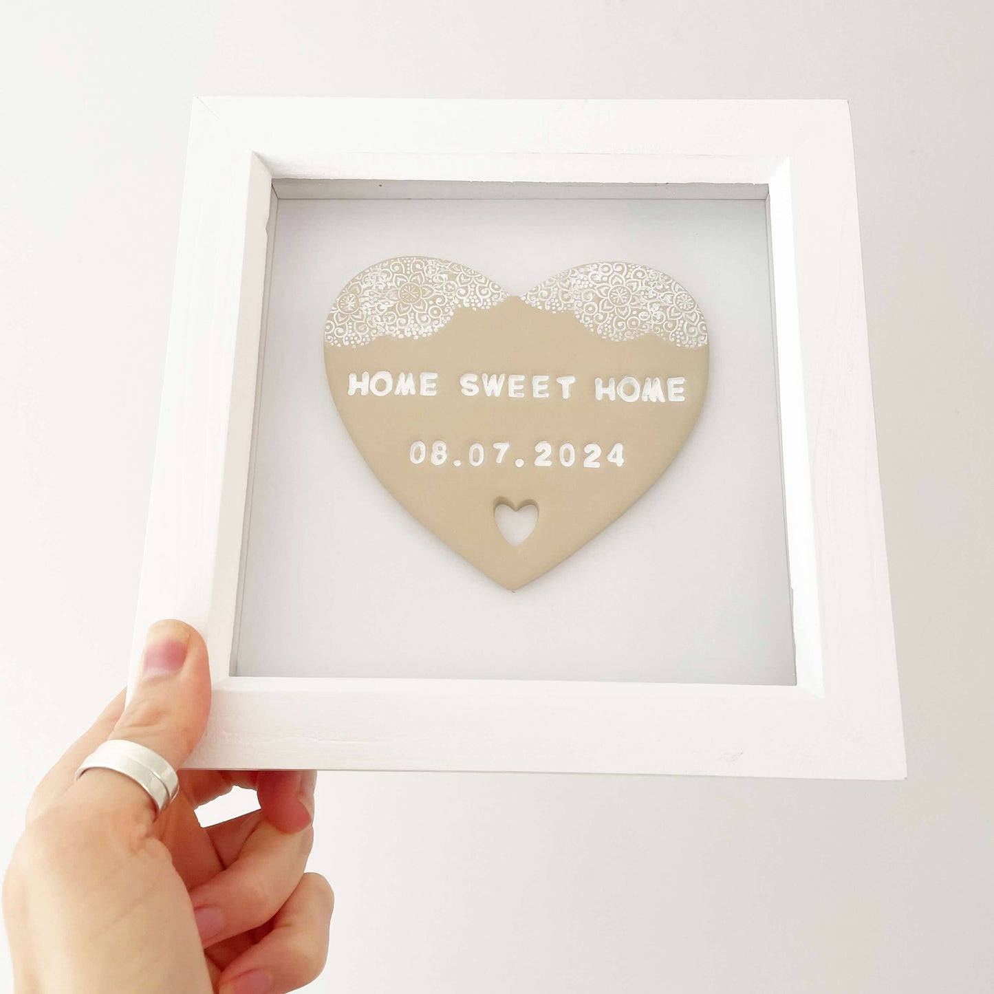 Personalised housewarming new home gift, beige clay heart with a white lace edge at the top of the heart and a heart cut out at the bottom in a white box frame, the heart is personalised with HOME SWEET HOME 08.07.2024