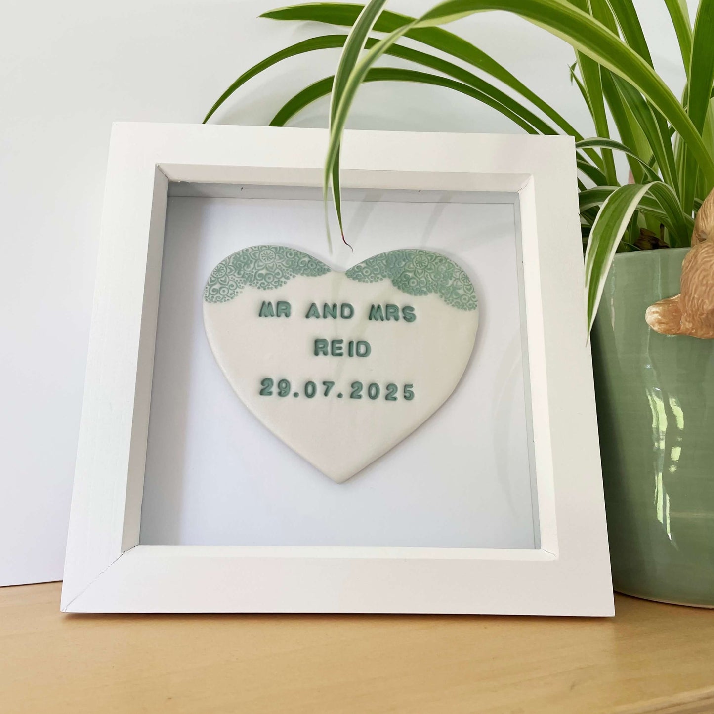 Personalised framed wedding heart gift, pearlised white clay heart with a sage green lace edge at the top of the heart in a white box frame, the heart is personalised with MR AND MRS REID 29.07.2025