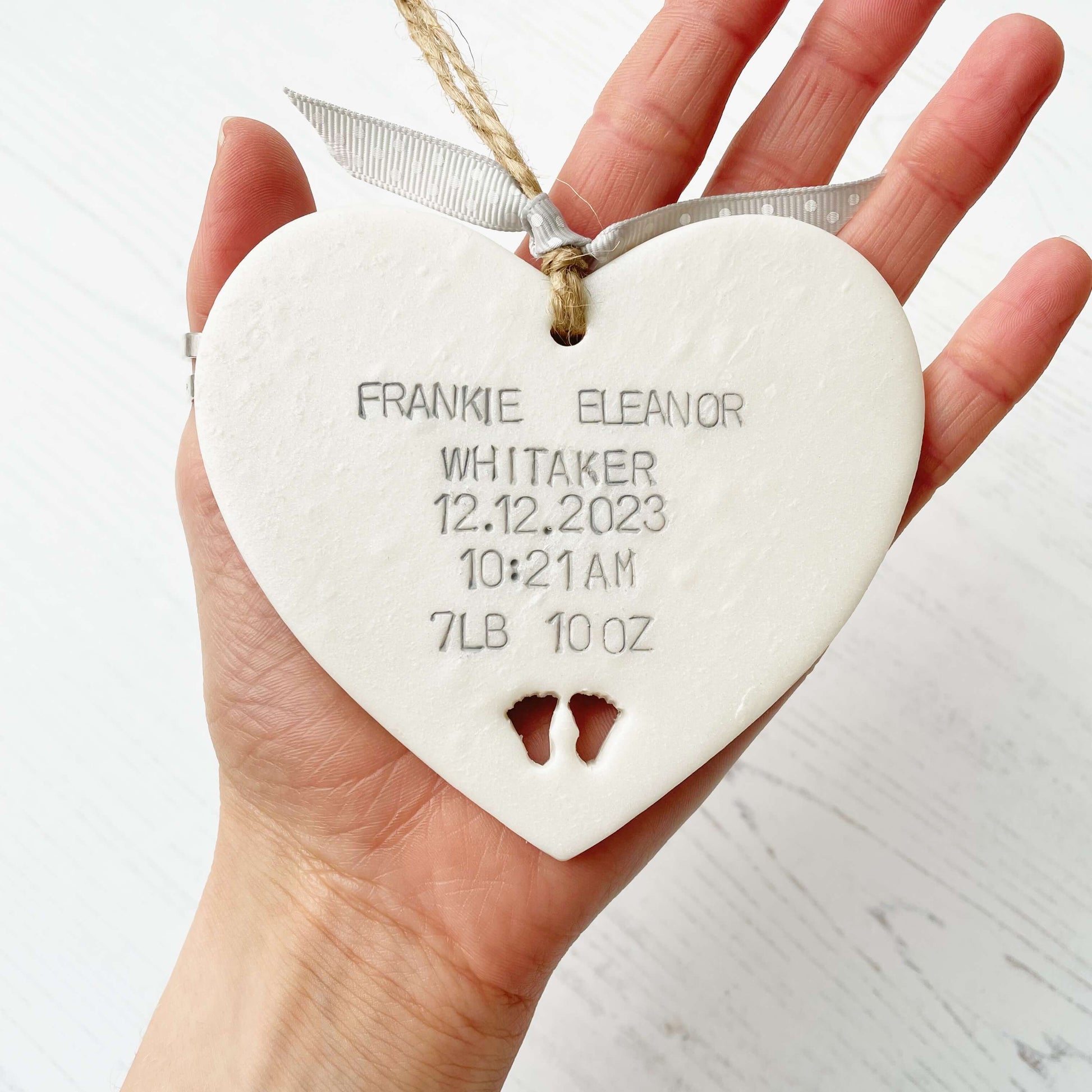 Personalised baby keepsake gift, pastel pearlised white hanging clay heart with baby feet cut out at the bottom of the heart, the heart is personalised with the baby’s name, date of birth, weight and time