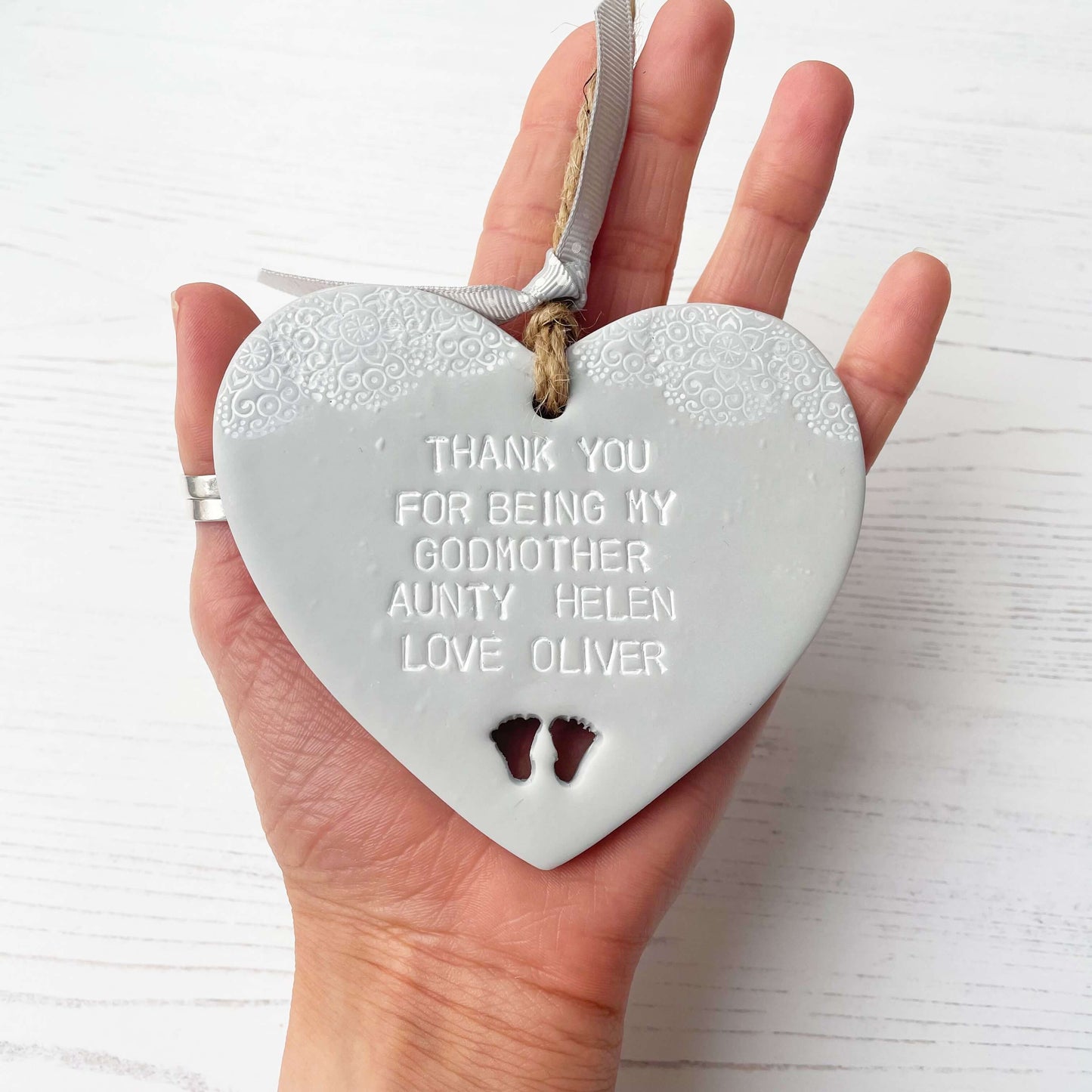 Personalised Godmother gift, grey clay hanging heart with baby feet cut out of the bottom and white lace edge at the top of the heart, the heart is personalised with THANK YOU FOR BEING MY GODMOTHER HELEN LOVE OLIVER