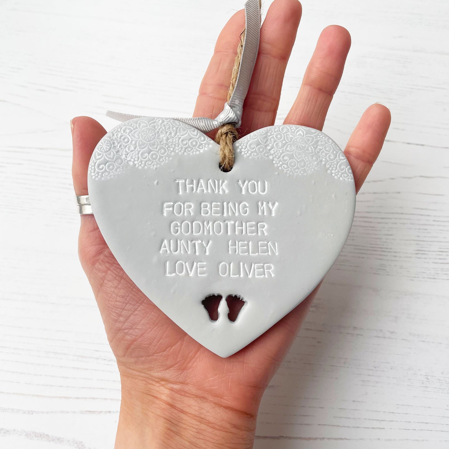 Personalised Godmother gift, grey clay hanging heart with baby feet cut out of the bottom and white lace edge at the top of the heart, the heart is personalised with THANK YOU FOR BEING MY GODMOTHER HELEN LOVE OLIVER