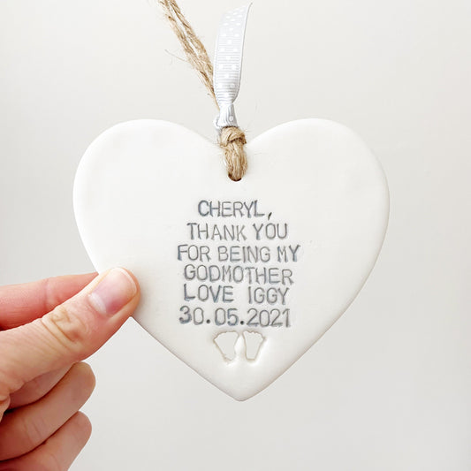 Personalised Godmother gift, pearlised white clay hanging heart with baby feet cut out of the bottom, the heart is personalised with CHERYL, THANK YOU FOR BEING MY GODMOTHER LOVE IGGY 30.05.2021