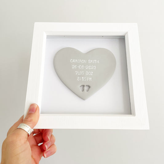 Personalised baby keepsake gift, grey clay heart with baby feet cut out at the bottom of the heart in a white box frame, the heart is personalised with the baby’s name, date of birth, weight and time