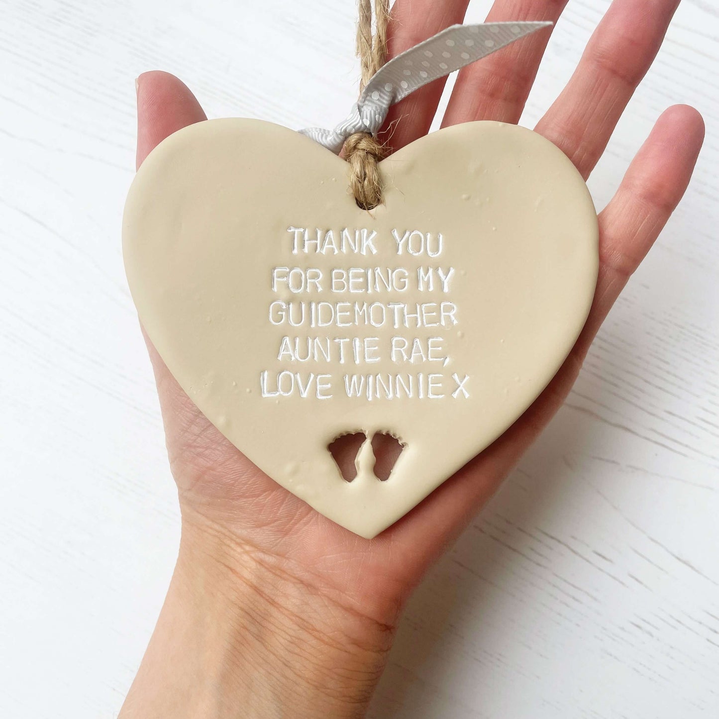 Personalised Guide parent gift, beige clay hanging heart with baby feet cut out of the bottom, the heart is personalised in white with THANK YOU FOR BEING MY GUIDEMOTHER AUNTIE RAE, LOVE WINNIE X