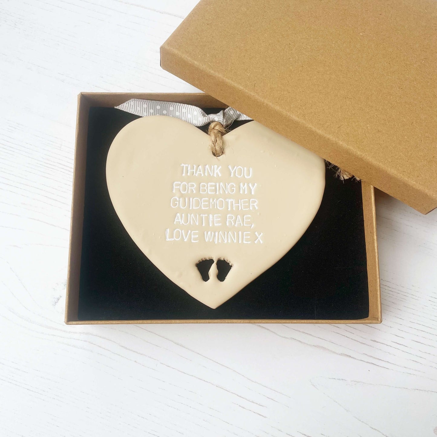 Personalised Guide parent gift, beige clay hanging heart with baby feet cut out of the bottom, the heart is personalised in white with THANK YOU FOR BEING MY GUIDEMOTHER AUNTIE RAE, LOVE WINNIE X