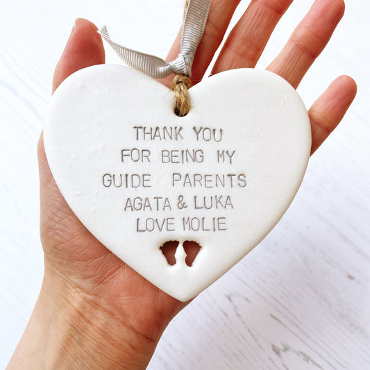 Personalised guide parent gift, pearlised white clay hanging heart with baby feet cut out of the bottom, the heart is personalised with THANK YOU FOR BEING MY GUIDE PARENTS AGATA & LUKA LOVE MOLIE