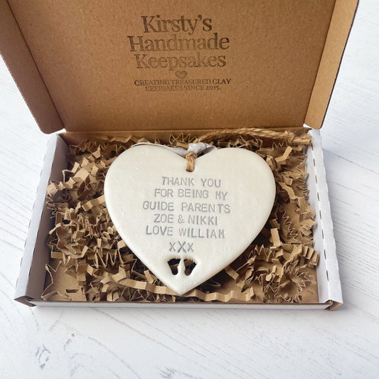 Personalised guide parents gift, pearlised white clay hanging heart with baby feet cut out of the bottom, the heart is personalised with THANK YOU FOR BEING MY GUIDE PARENTS ZOE & NIKKI LOVE WILLIAM xXx In a postal box with brown Kraft shredded zigzag paper
